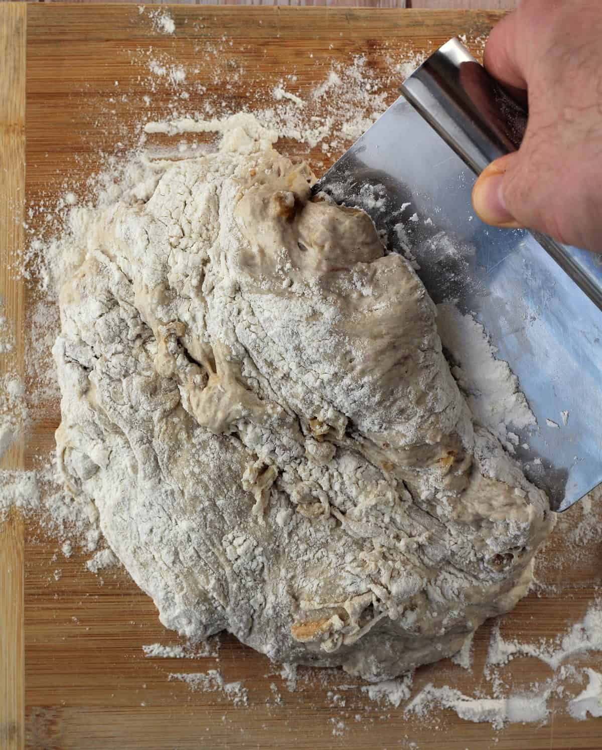 No knead fig walnut bread dough scraped onto a floured wood board with bench scraper.
