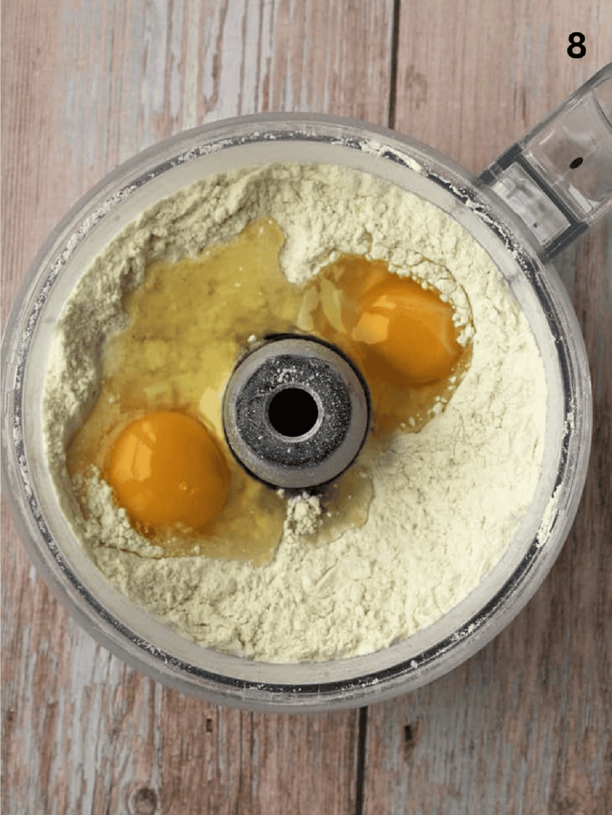 Two eggs added to food processor bowl with dry ingredients for shortcrust dough.