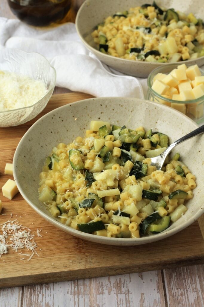 Spoon in bowl of risotto-style pasta with zucchini on wood board with cheese.