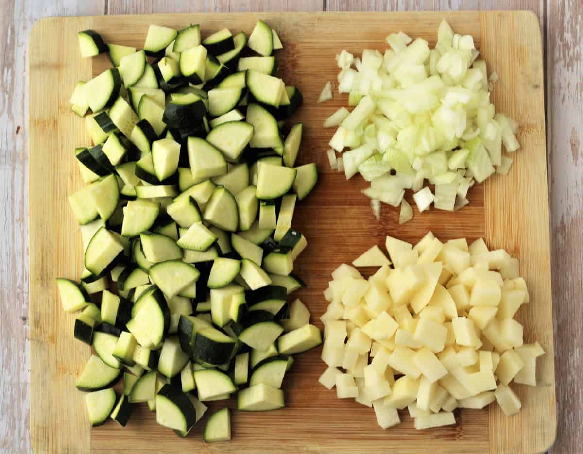 DIced zucchini, onion and potato on wood board.