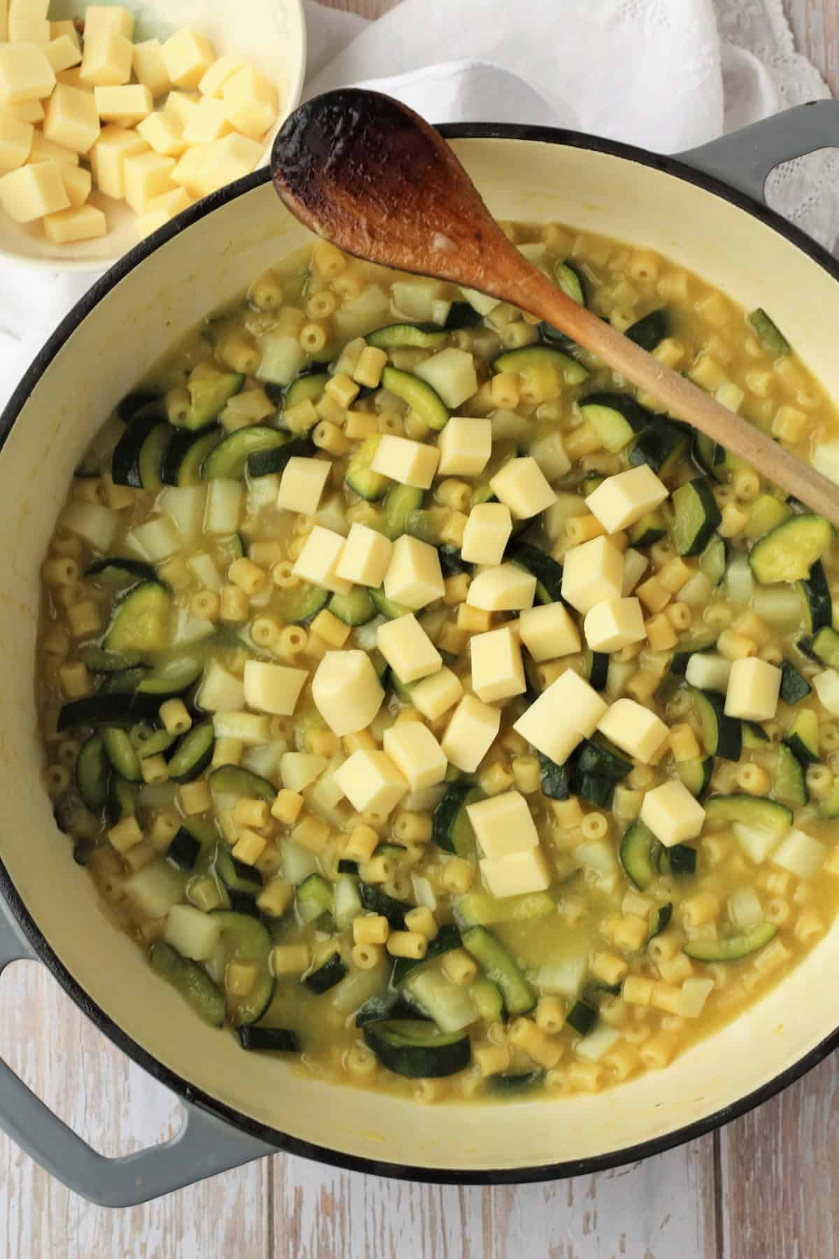 Risotto pasta with zucchini and cubed cheese added to skillet.