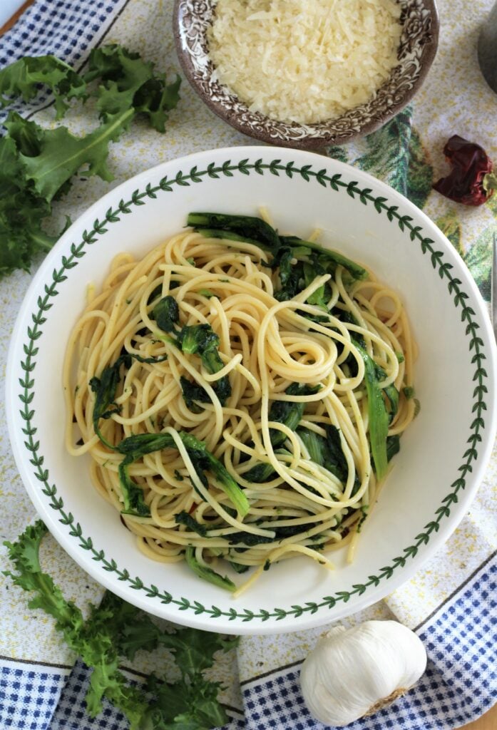 Bowl full of spaghetti and escarole with escarole leaves, garlic bulb and cheese bowl around it.