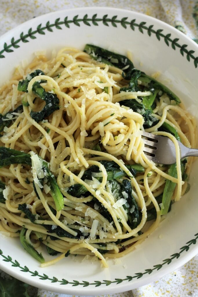 Forkful of escarole pasta topped with cheese in bowl.