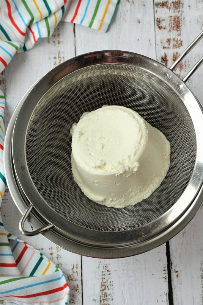 Ricotta draining in fine mesh sieve over bowl.