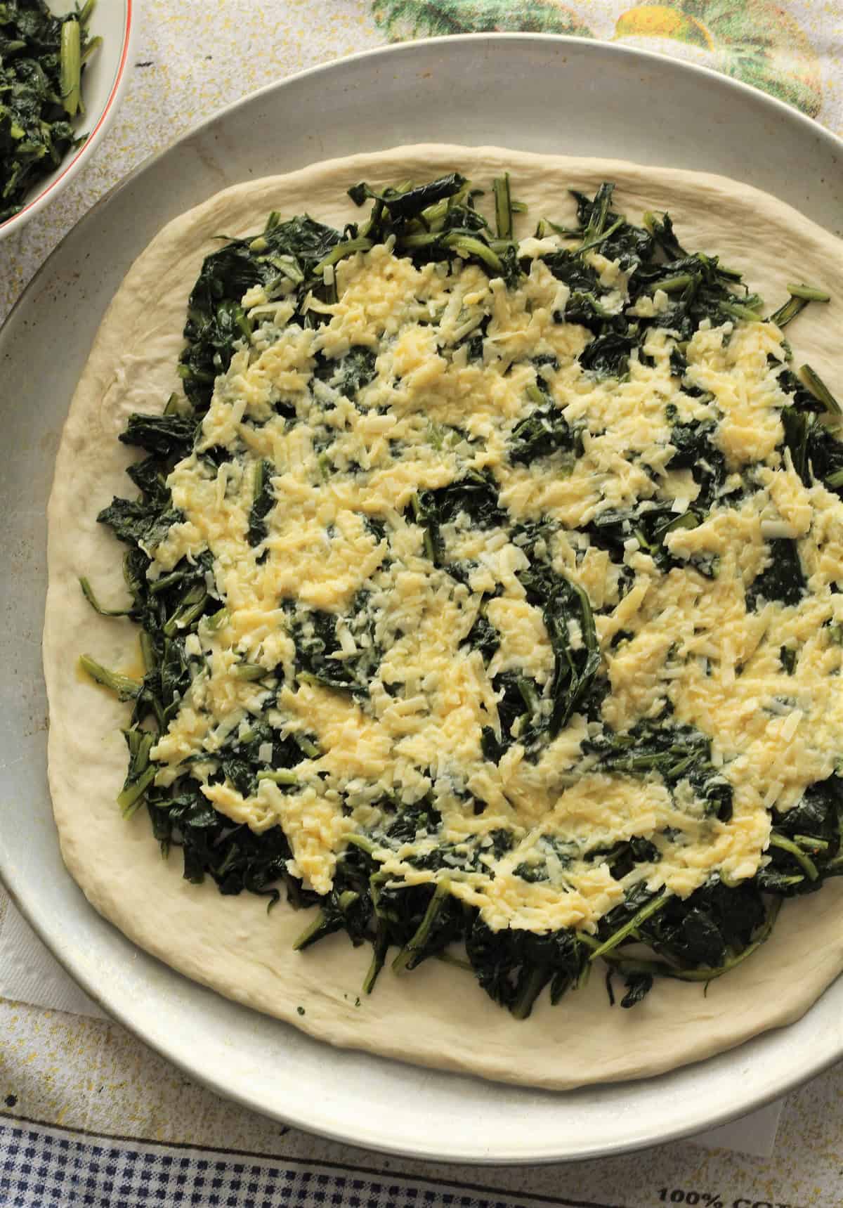 Pizza dough topped with chicory, egg and parmigiano cheese on pizza pan.