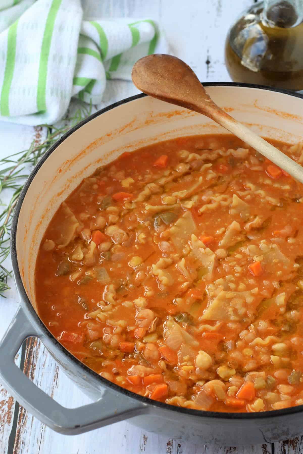 Creamy chickpeas with pasta in pan with wooden spoon.