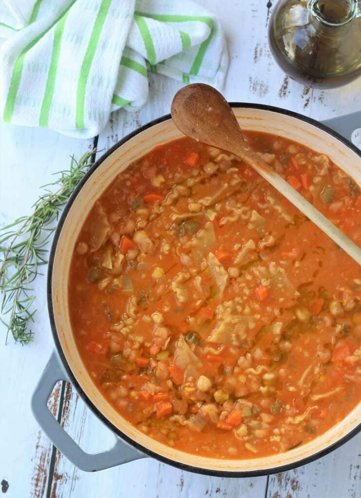 Creamy chickpeas with pasta in large pan with wooden spoon.