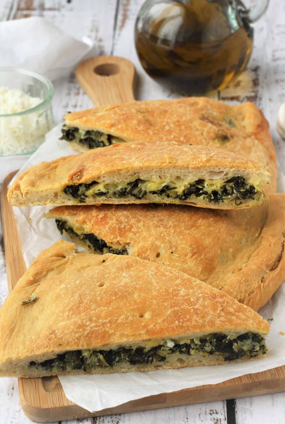 Wedges of cicoria stuffed pizza on wood board with olive oil bottle.