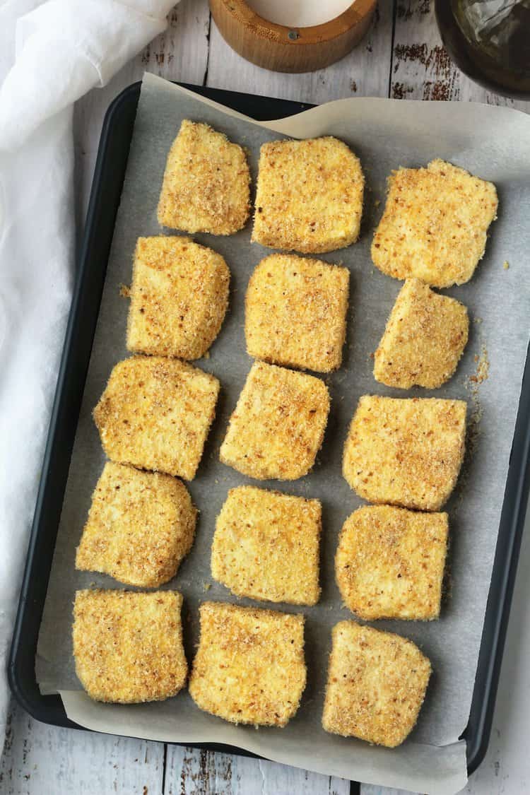 Breaded tuma cheese squares on baking sheet.