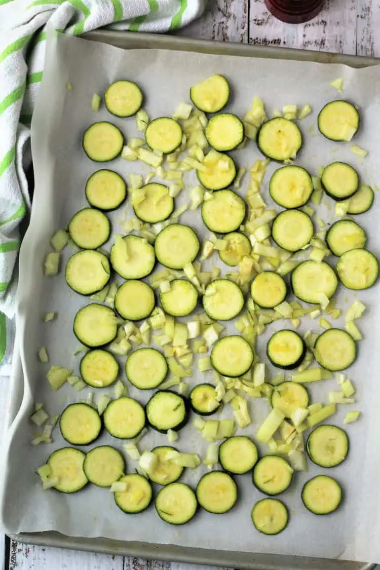 Zucchini rounds and diced onion on baking sheet.