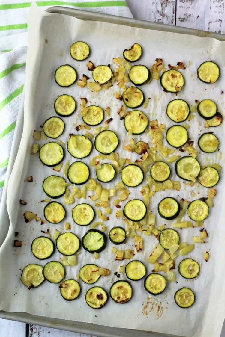 Roasted zucchini rounds with onion on baking sheet.