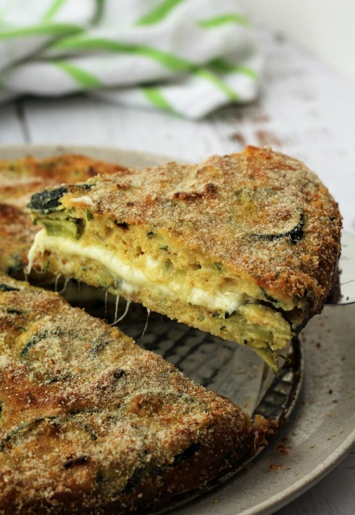 Wedge of cheesy zucchini frittata on spatula.