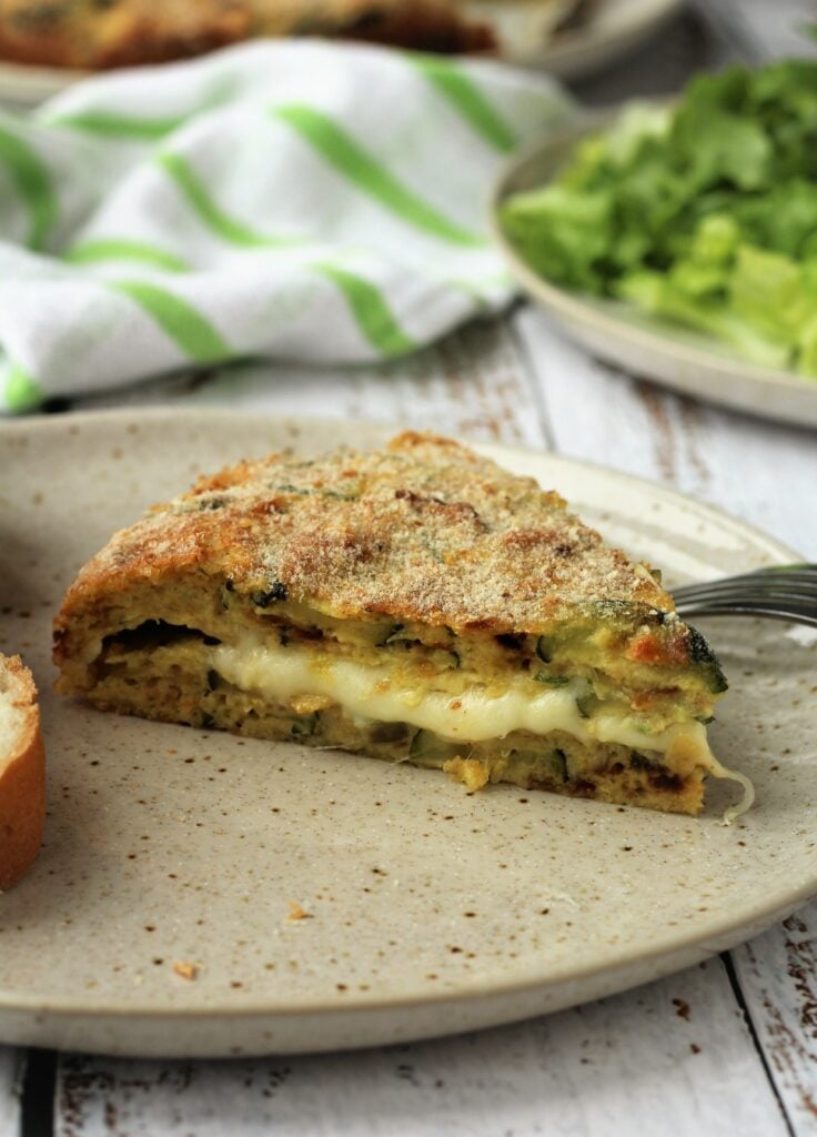 Wedge of cheese filled zucchini frittata on plate.