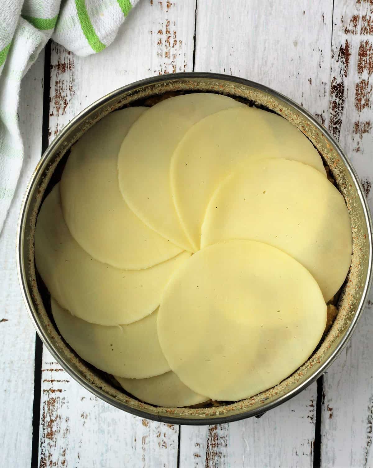 Overlapping provolone cheese slices on zucchini egg mixture in springform pan.