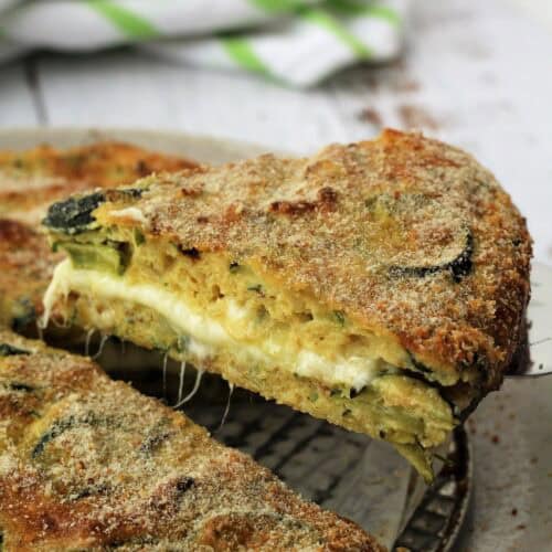 Slice of cheesy baked zucchini frittata served with spatula.