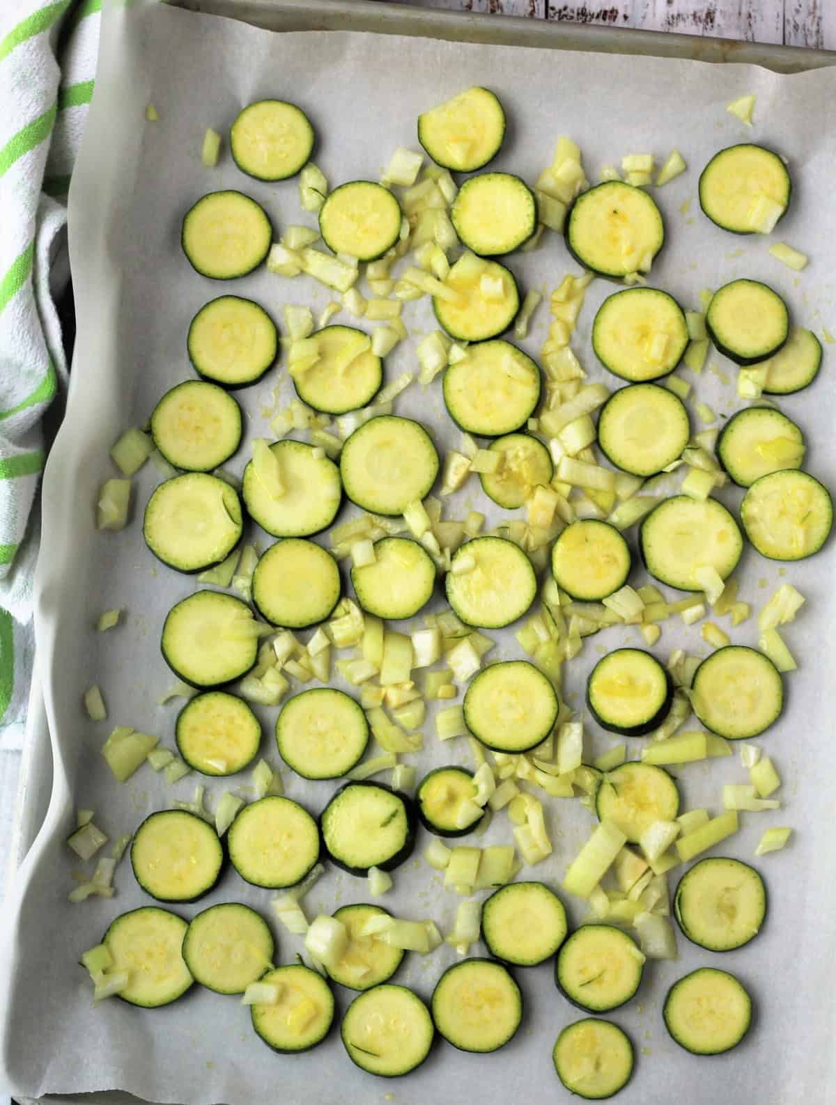 Sliced zucchini and onions on baking sheet coated with olive oil.