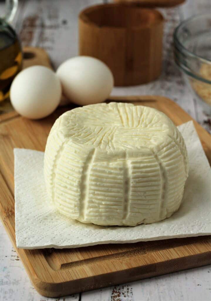 Whole tuma cheese on wood board next to eggs.