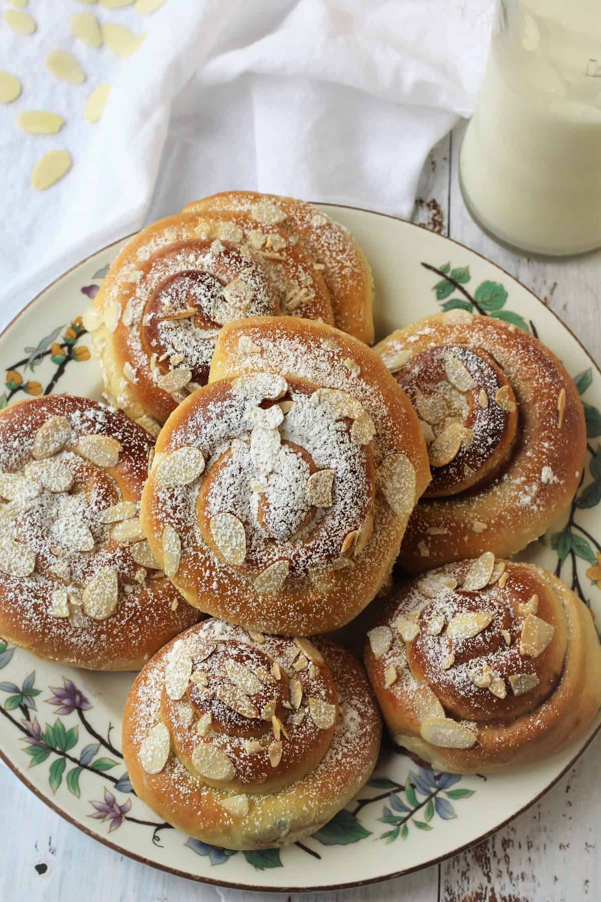 Brioche swirls filled with jam and almonds piled on plate and bottle of milk next to it.