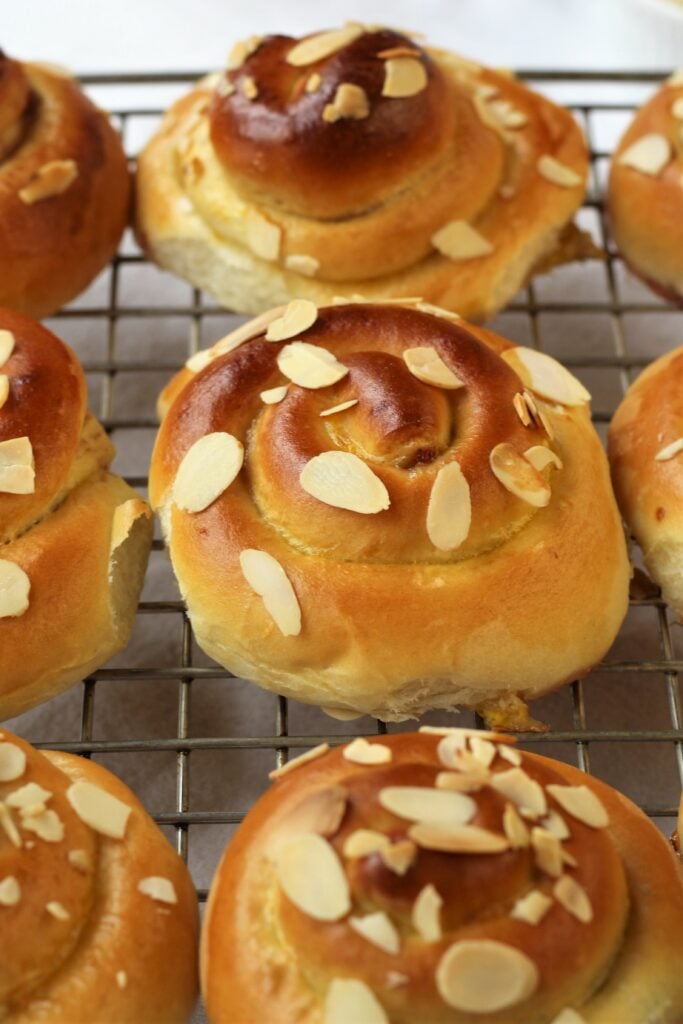 Baked brioche swirls topped with almonds on wire rack.