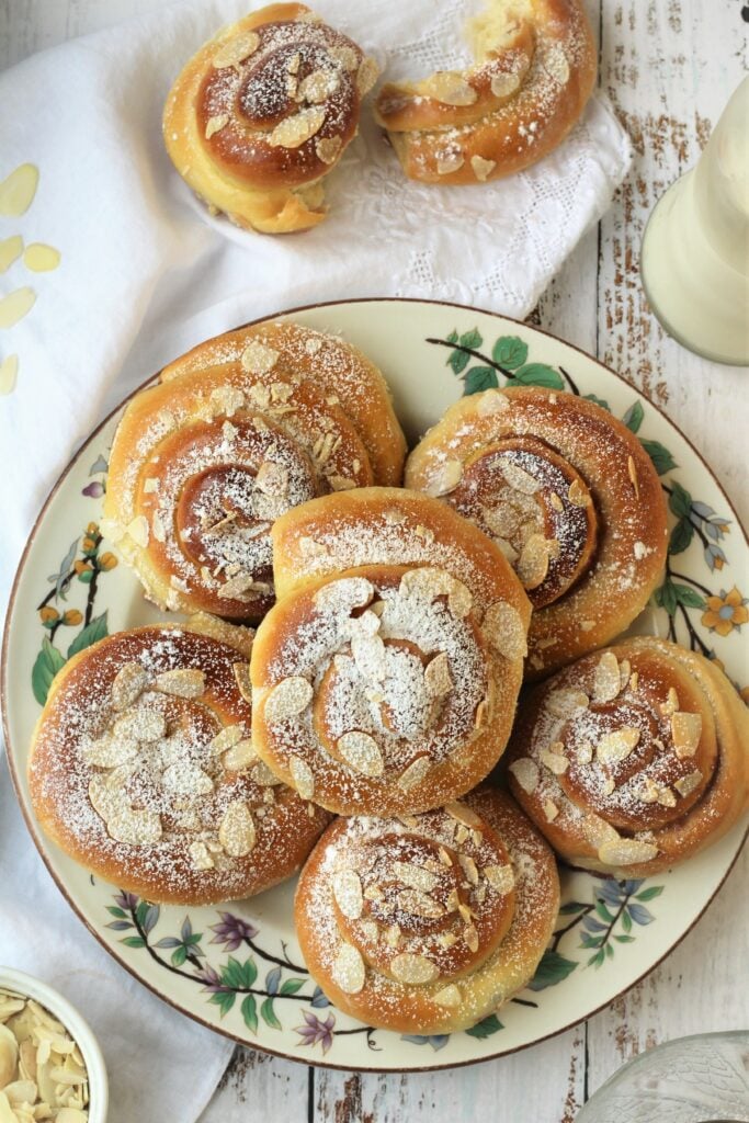Brioche swirls topped with almonds on round plate.