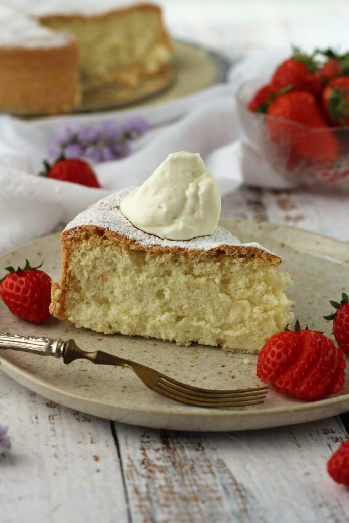 Slice of gluten free pan di spagna cake with whipped cream and strawberries.