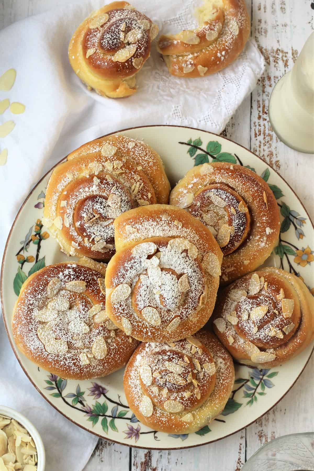 Brioche swirls with jam and topped with almonds on plate with one cut in half next to plate.