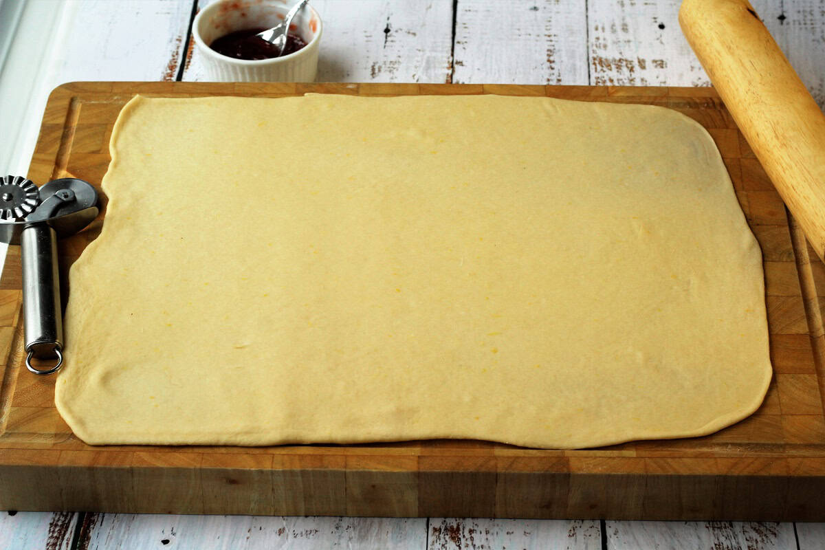 Brioche dough flattened in large rectangle on wood board with rolling pin.