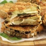 Melanzane in carrozza sandwiches on wood board with basil leaves.