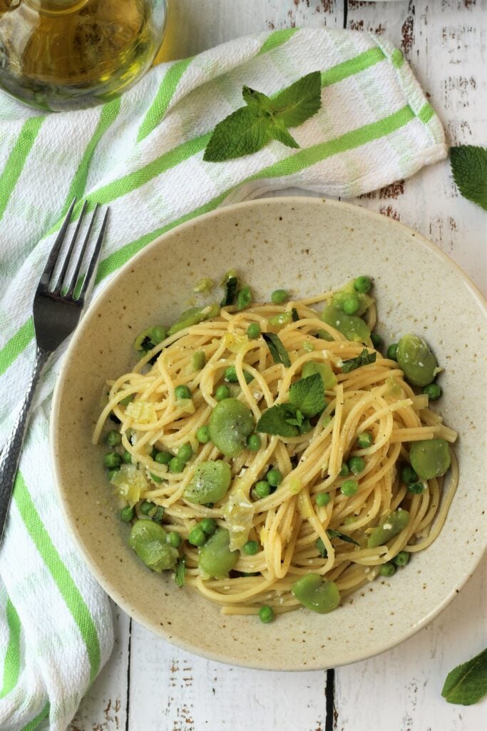 Bowl of spaghetti with fava beans, peas and mint with fork on side.