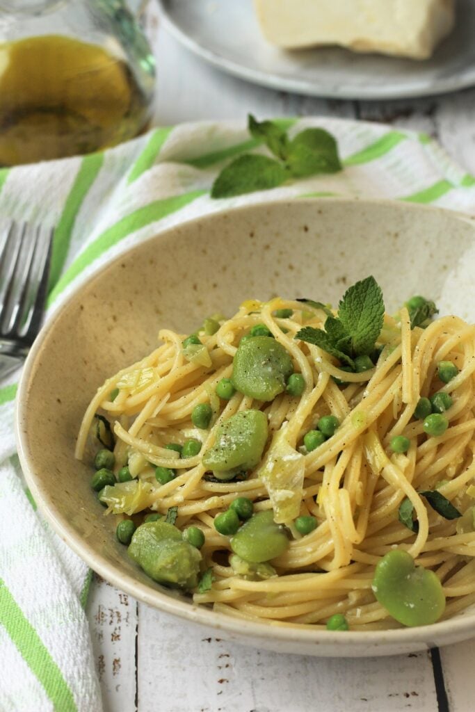 Bowl with spaghetti and fava beans and peas topped with mint.