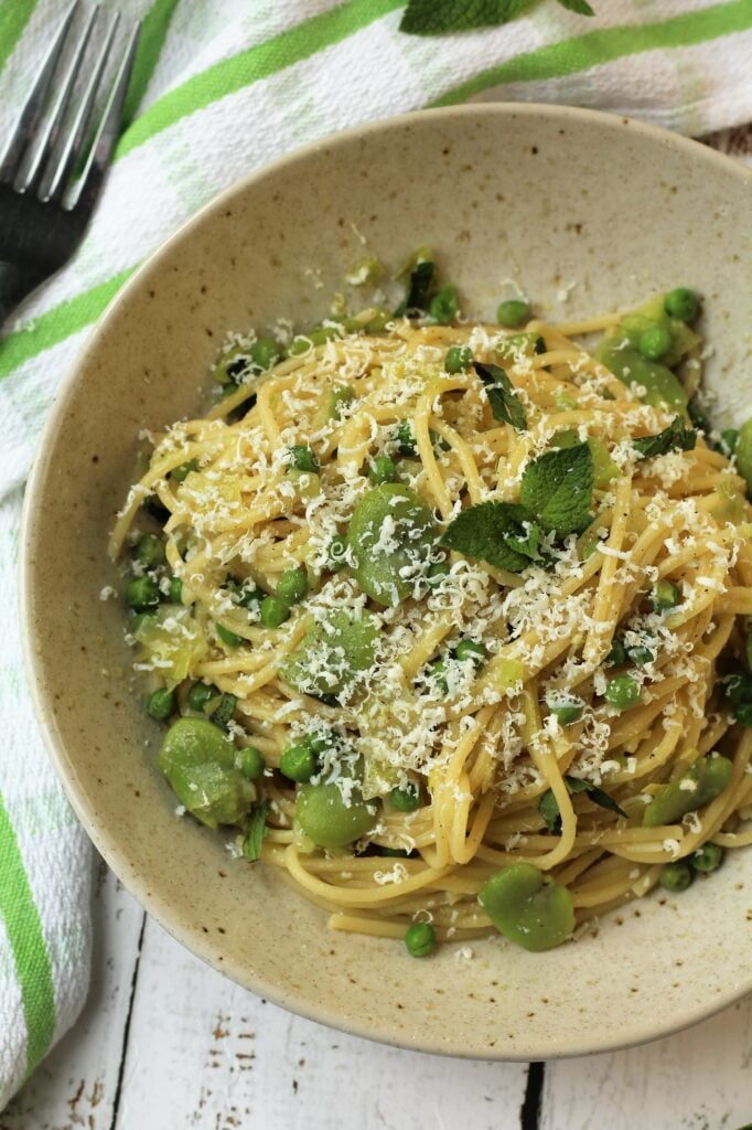 Bowl with spaghetti, fava benas and peas topped with ricotta salata and mint.