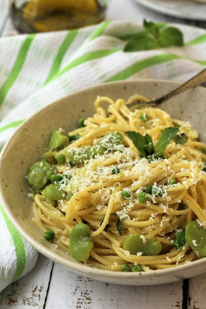 Plate of spaghetti with fava beans and peas with grated cheese.