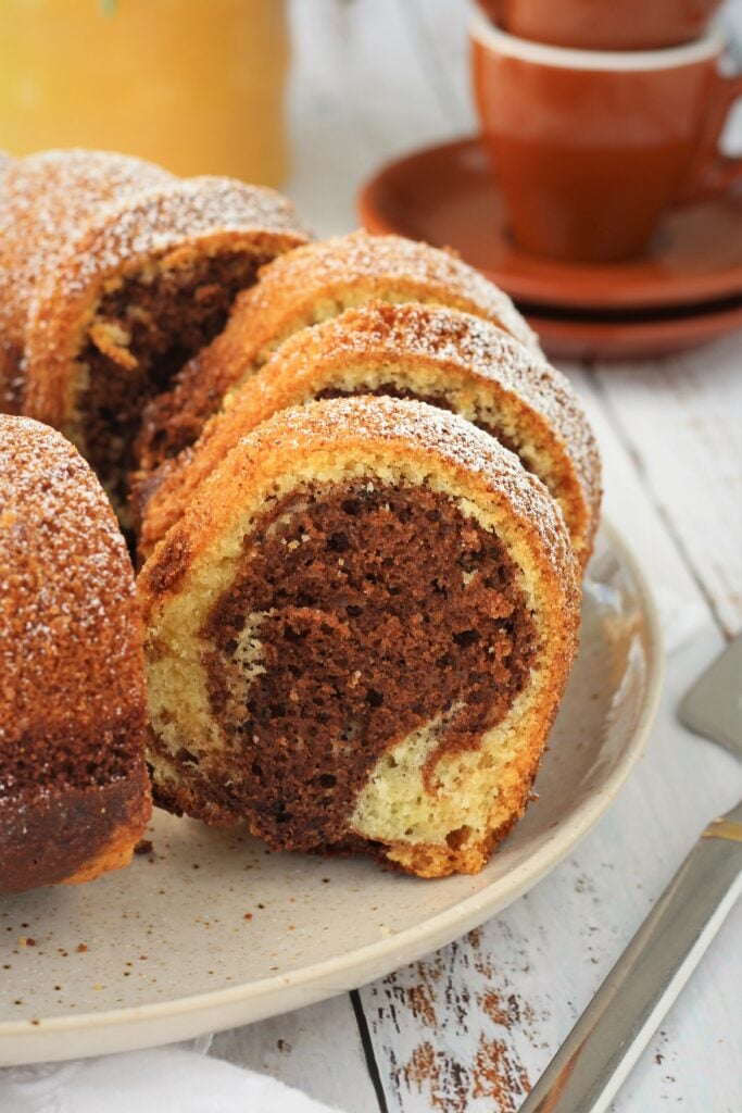 Sliced cjocolate marble bundt cake on plate with coffee cups.