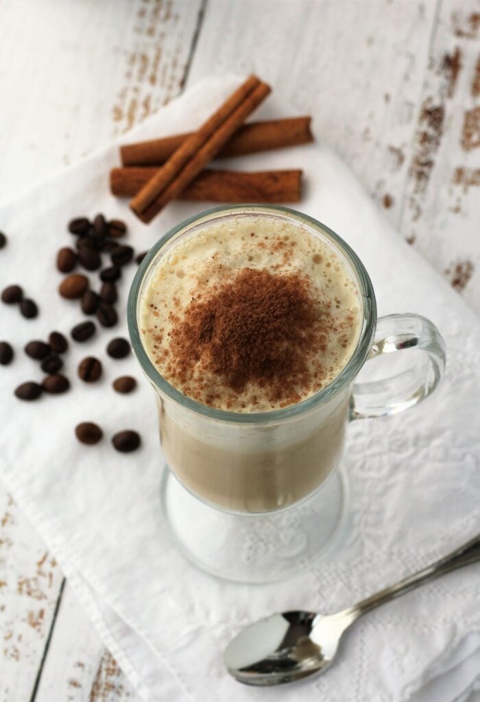 Iced cappuccino in glass with coffee beans and cinnamon sticks on side.