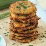 Piled crispy Italian zucchini fritters on wood board topped with chives.