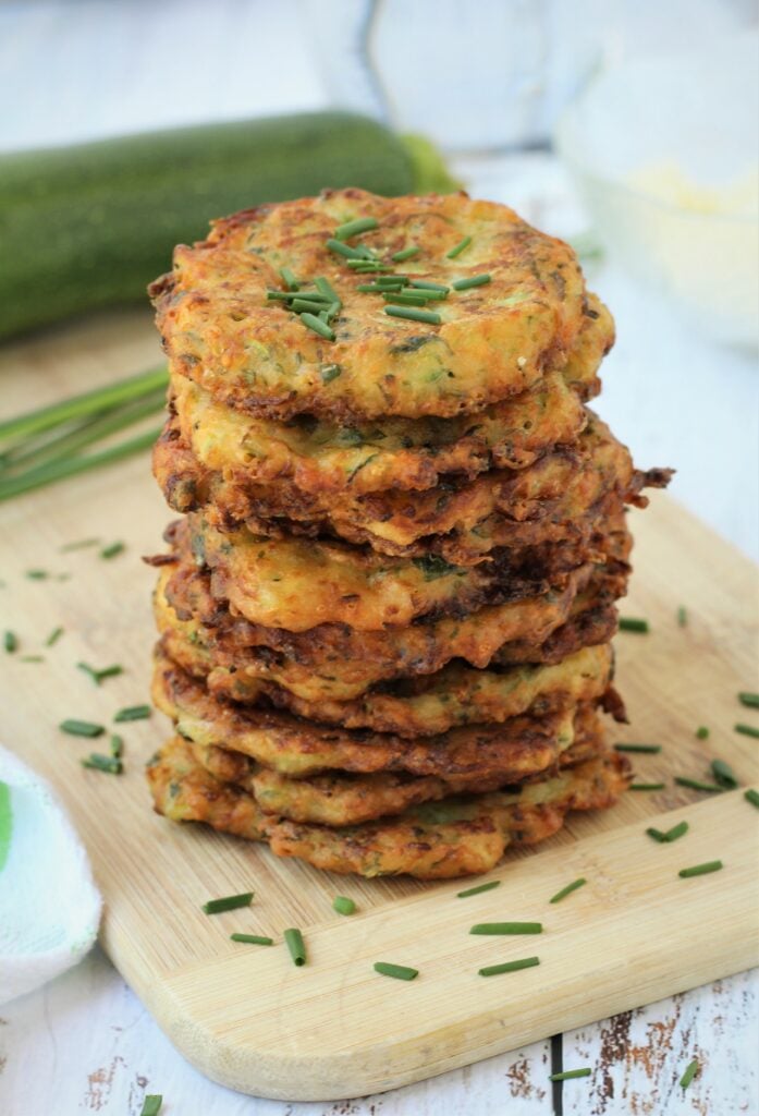 Piled crispy Italian zucchini fritters on wood board topped with chives.