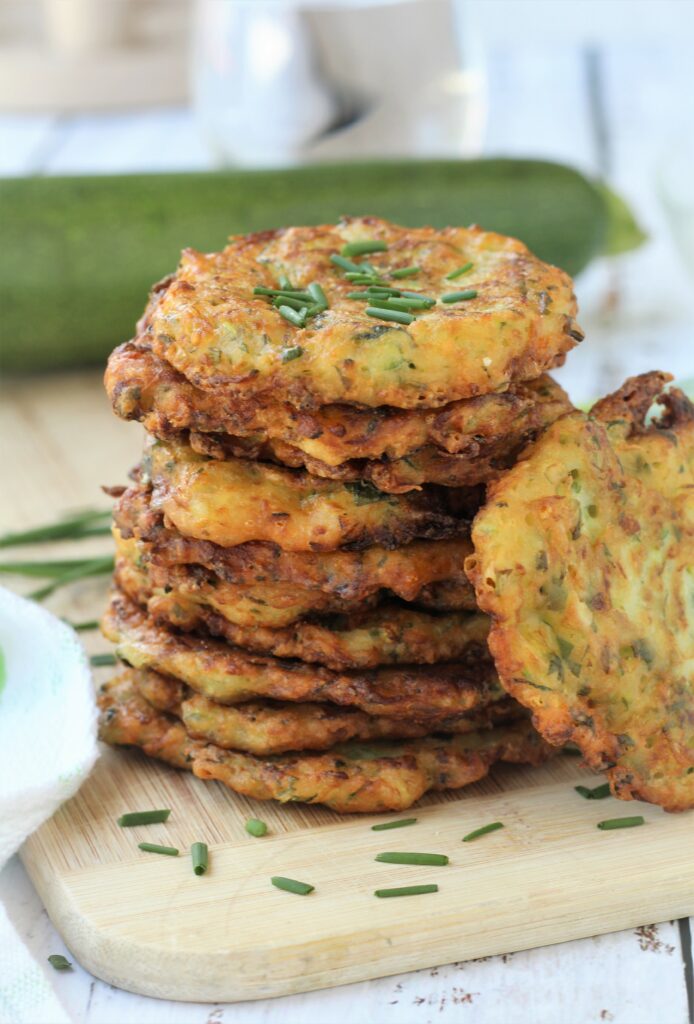 PIled Italian zucchini fritters on wood board with zucchini in background.
