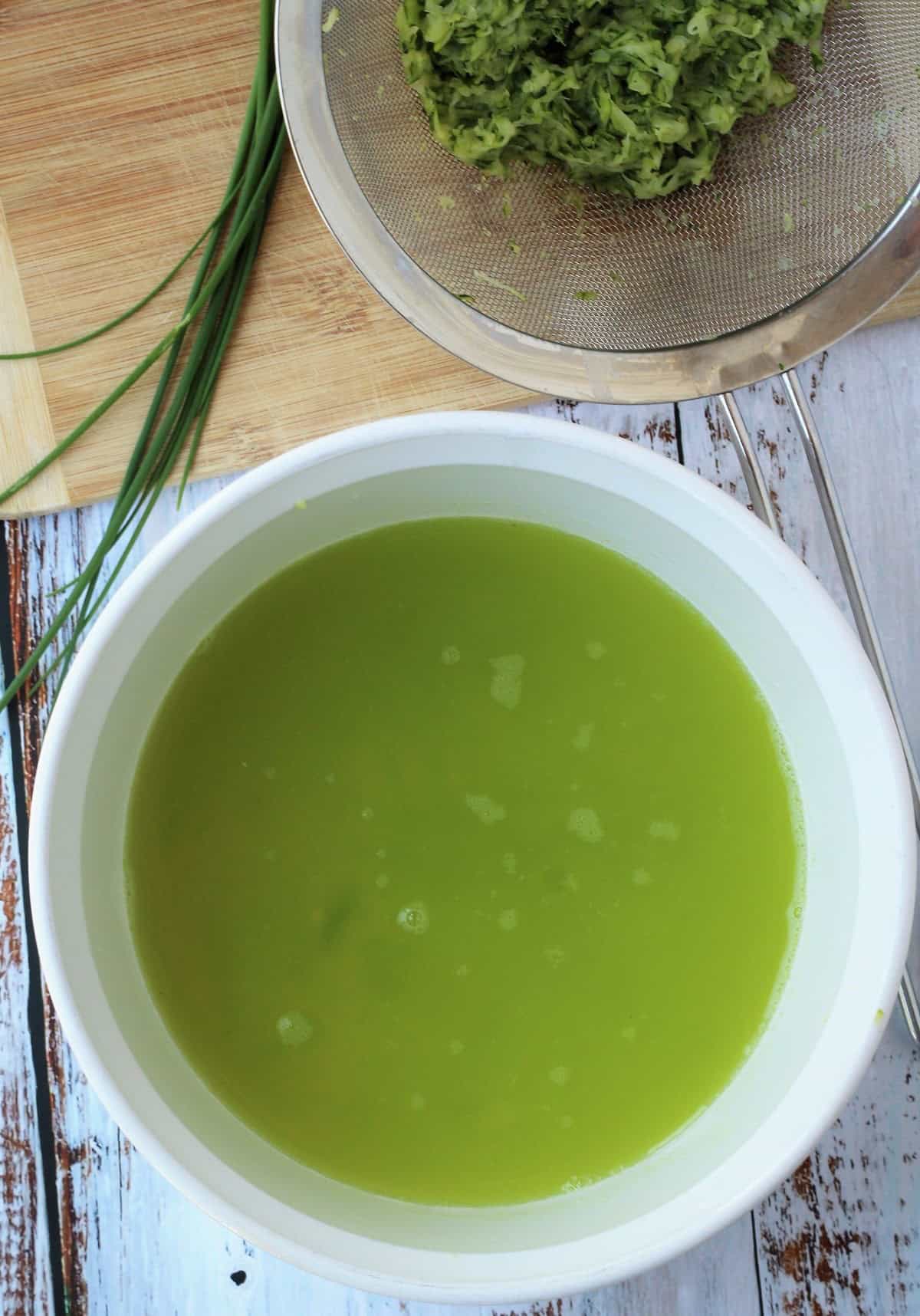 Zucchini water drained from shredded zucchini in sieve for fritters.
