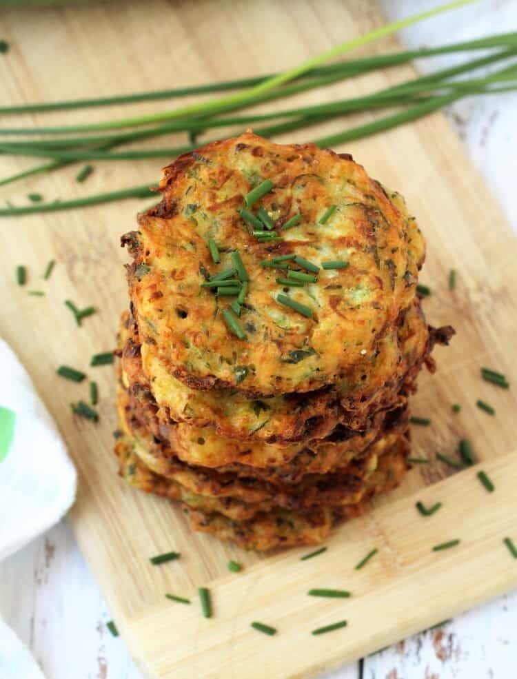 Crispy Italian zucchini fritters piled on wood board and garnished with chopped chives.