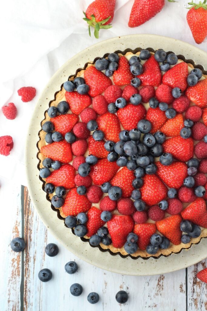 Berry topped fruit tart in pan with berries around it.