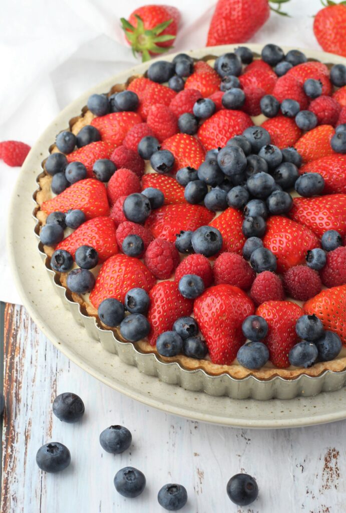 Fruit tart with pastry cream in tart pan on plate.