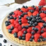Fruit tart with custard filling on plate with blueberries around it and spatula.