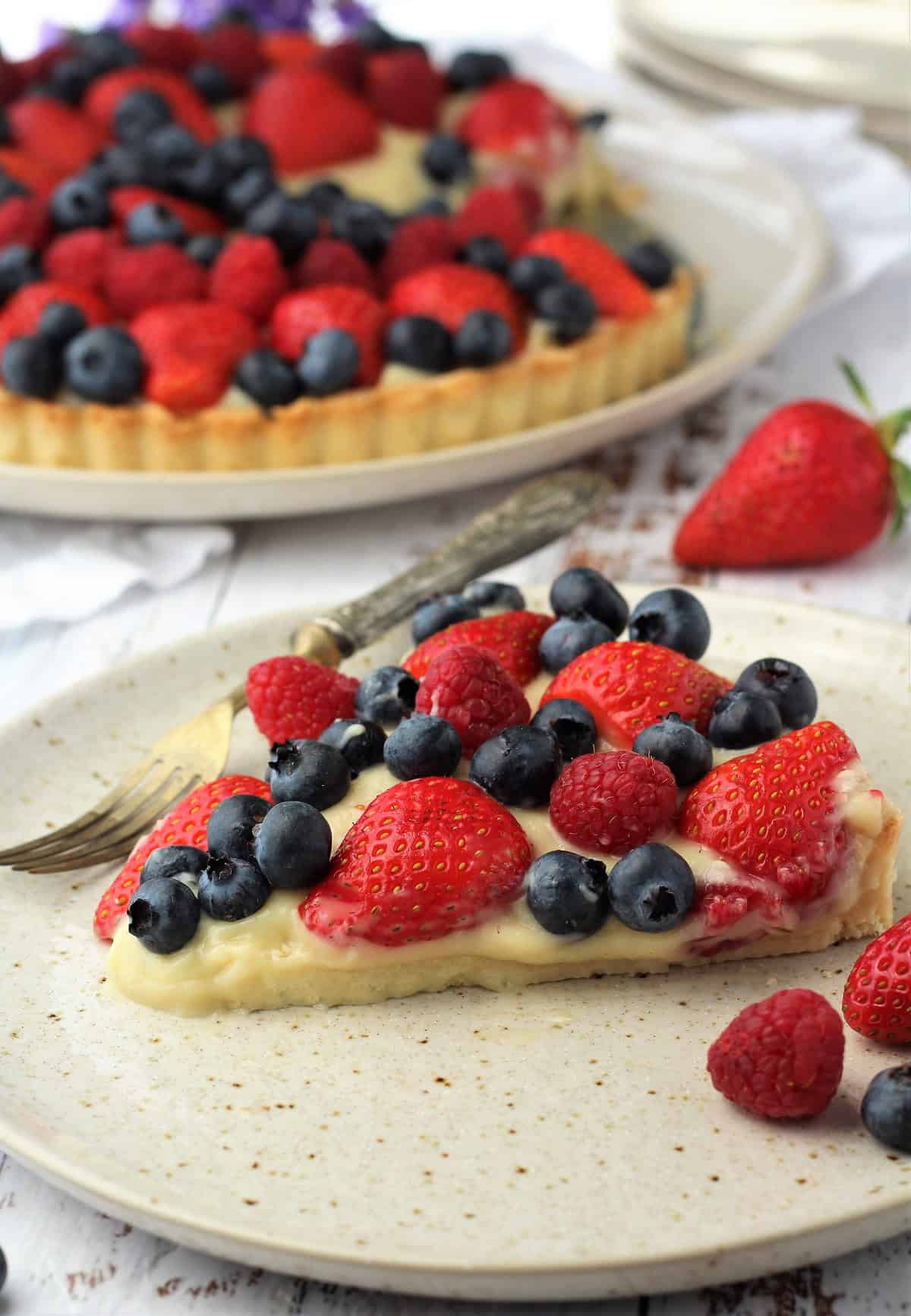 Wedge of Italian fruit tart with pastry cream topped with berries on round plate with fork.