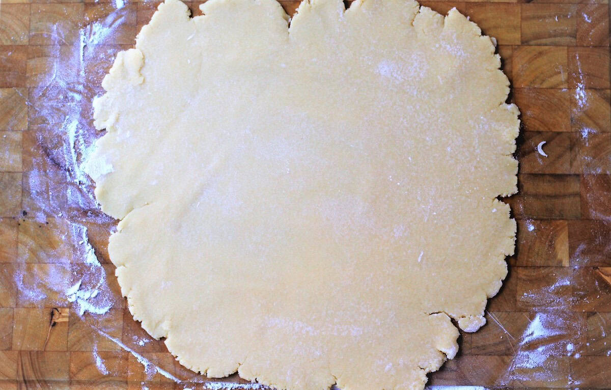 Flattened pastry dough into circular shape on wood board.