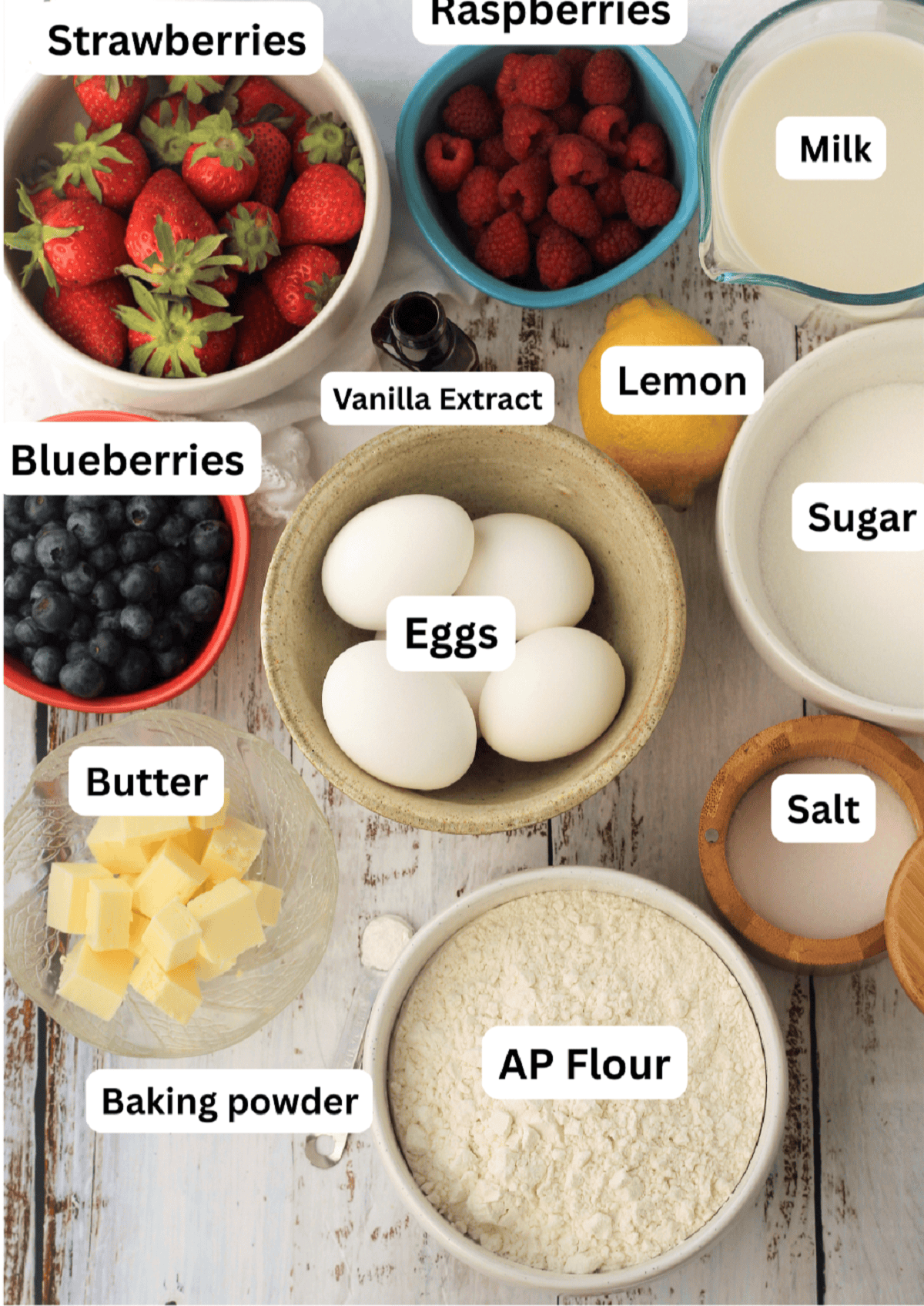 Berries in bowls, flour, eggs, milk, lemon ,salt flour, butter, baking powder, vanilla extract.
