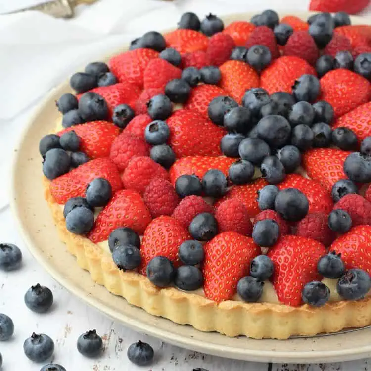 Fruit tart topped with berries on round plate.