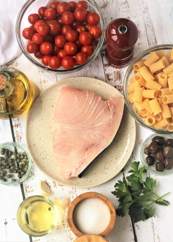 Swordfish on plate, cherry tomatoes, pasta, parsley, olives, capers, salt, pepper and olive oil.