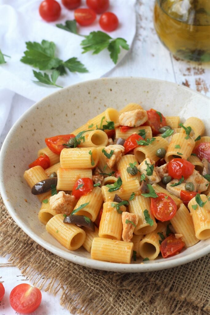 Bowl of pasta with swordfish with cherry tomatoes, parsley and olive oil bottle on side.