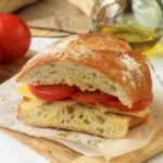 Sicilian pane cunzatu sandwich with tomatoes and cheese on wood board.