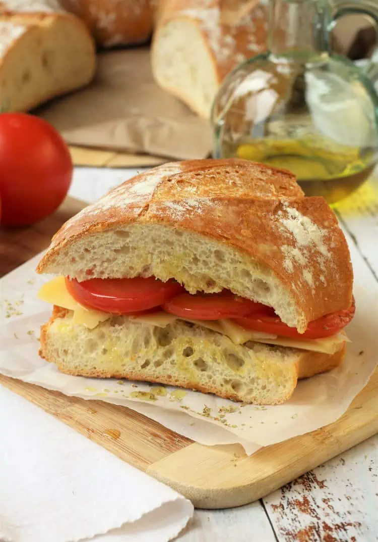 Sicilian pane cunzatu sandwich with tomatoes and cheese on wood board.
